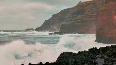Portekiz 'in Azores şehrinde fırtınalı bir günde Sao Miguel adasının dramatik sahillerine Atlantik okyanus dalgaları çarpar. Güçlü doğal deniz manzarası dalgalı deniz enerjisini ve vahşi kıyı manzarasını gösteriyor. Yavaş çekim