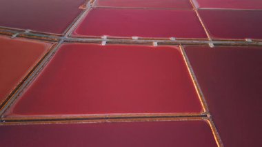 Margherita di Savoia tuz madenlerinin günbatımında Puglia, İtalya 'daki hava manzarası, Avrupa' nın en büyük tuz madencilik kompleksinin renkli pembe buharlaşma alanlarını ve geometrik göletlerini gösteriyor.