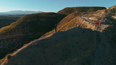 Kadın yürüyüşçü, gün batımında bir dağın zirvesinde durmuş İspanya 'nın Endülüs kentindeki Gorafe Çölü' nün dağlık çöl manzarasının dramatik ışığını seyrediyor. Hava aracı görünümü
