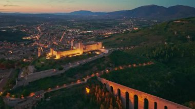 Ortaçağ Spoleto 'sunun dramatik hava manzarası, Umbria' nın geceleri. İtalya 'da şehir ışıkları altında parıldayan Ponte delle Torri su kemeri ve Rocca Albornoziana kalesi yer alıyor..