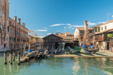 Venedik, İtalya. Tarihi tuğla binalar ve ahşap barakalarla dolu sessiz bir kanal boyunca gondolların inşa edilip onarıldığı geleneksel bir filo ya da tersane manzarası..