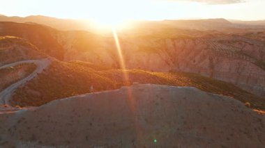 Gün batımında bir dağ zirvesinde yürüyen bayan yürüyüşçü İspanya 'nın Endülüs kentindeki Gorafe Çölü' nün dağlık çöl manzarasında dramatik ışığı seyrediyor. Hava aracı görünümü