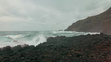 Portekiz 'in Azores şehrinde fırtınalı bir günde Sao Miguel adasının dramatik sahillerine Atlantik okyanus dalgaları çarpar. Güçlü doğal deniz manzarası dalgalı deniz enerjisini ve vahşi kıyı manzarasını gösteriyor. Yavaş çekim