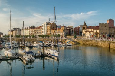 Gijon, İspanya - 19 Temmuz 2024: Limanda demirli yatlar ve yelkenlilerin yer aldığı liman manzarası ve arka planda eski kasaba mimarisi. Gijon, Asturias, İspanya