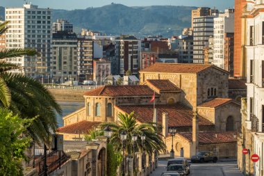 Gijon, Asturias, İspanya kıyılarında yer alan San Pedro Kilisesi 'nin manzarasında uzun bir çan kulesi ve taş mimarisi şehir binaları ve deniz manzarasına karşıdır..