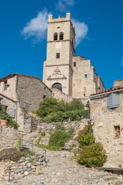 Fransa 'nın Eus kentindeki tarihi yamaç köyünde geleneksel taş evlerin üzerinde yükselen Romanesk Saint Vincent kilisesinin manzarası.