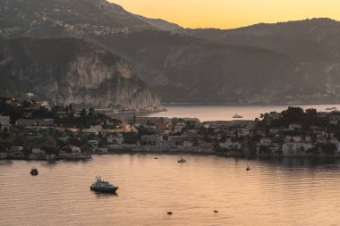 Sahil villaları ve alacakaranlıkta kireçtaşı dağları ile çevrili sakin koyda demirli lüks motor yatlarının günbatımı manzarası Saint-Jean-Cap-Ferrat, Fransa