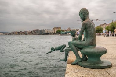 Santander, İspanya - 8 Ağustos 2024 Los Raqueros olarak bilinen bronz heykeller, bulutlu bir gökyüzünün altında Santander 'in deniz gezintisinde yer alan erkek çocukları temsil ediyor..