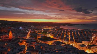 İtalya 'nın Puglia kentinde gece vakti Vieste Ortaçağ kasabasının havadan görünüşü, aydınlatılmış tarihi mimarisi, kıyı kayalıkları ve karanlık deniz manzarası ile Akdeniz üzerindeki atmosferik tatil beldesi