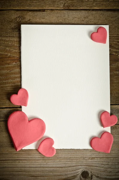 Carta bianca con piccoli cuori rosa sdraiati su uno sfondo di legno — Foto Stock