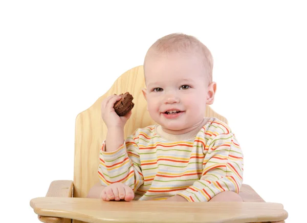 Leuke jongen zittend op een stoel en eten van cookie — Stockfoto