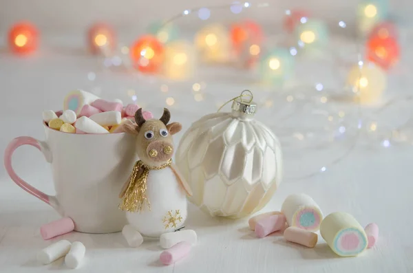 Witte Beker Met Marshmallows Een Speelgoedstier Een Wazige Achtergrond Kerstversiering — Stockfoto