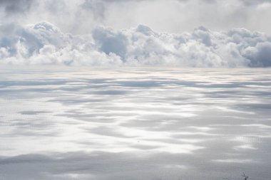 Güneş ışığı, bulutlar, gökyüzü ve deniz arasında.