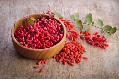 Barberry with leaves and dry goji berries on wooden background clipart