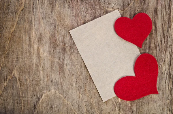 Dos corazones de tela roja con hoja de papel sobre fondo de madera viejo — Foto de Stock