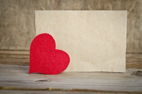 Corazón de tela roja con hoja de papel sobre una tabla de madera . —  Fotos de Stock