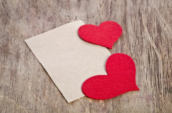 Two Red fabric hearts with sheet of paper lying on old wooden ba — Stock Photo, Image