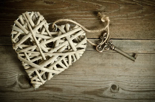 Corazón de mimbre hecho a mano con la llave acostada sobre una base de madera. arriba — Foto de Stock
