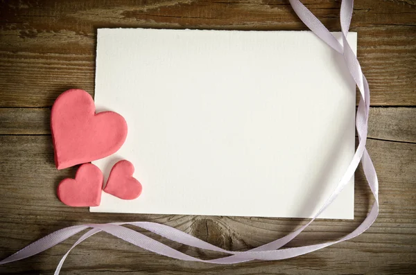 Het stuk van papier liegen met hartjes en linten op een houten bac — Stockfoto