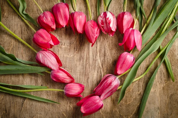 La cornice a forma di cuore di tulipani freschi è adagiata su un vecchio rusti — Foto Stock