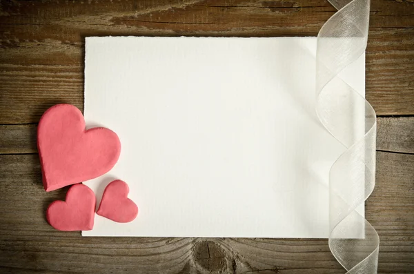 The piece of paper lying with hearts and ribbon on a wooden back — Stock Photo, Image