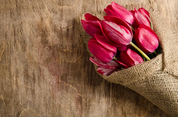 Beau bouquet de tulipes enveloppées de toile de jute sur la table en bois — Photo