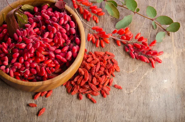 Barberry with leaves and dry goji berries on wooden background — Stock Photo, Image