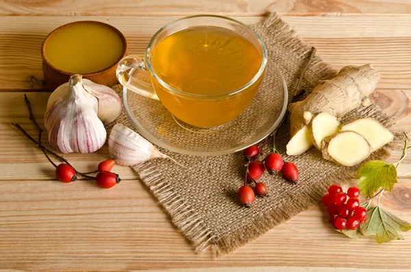 Чашка чая, ломтики имбиря, меда, ягод шиповника и вибурнума. — стоковое фото