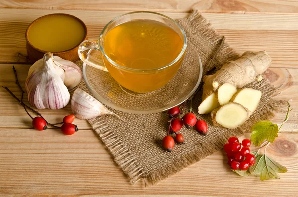 Чашка чая, ломтики имбиря, меда, ягод шиповника и вибурнума. — стоковое фото