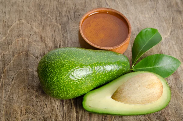 Aguacate fresco con hojas y tazón para aceite sobre fondo de madera — Foto de Stock