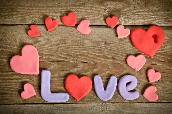 Palabra Composición de amor en la superficie del tablero de madera y muchos corazones — Foto de Stock