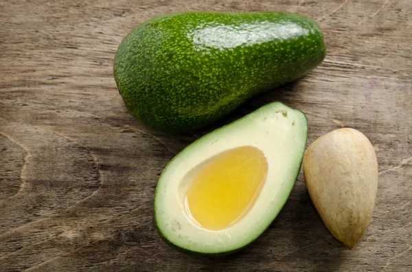 Aguacate fresco y la mitad de aguacate como un tazón para el aceite en madera — Foto de Stock