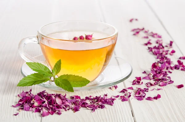 Glas kopje thee met mint en gedroogde rozenblaadjes op witte houten — Stockfoto