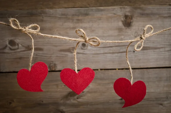 Trois coeurs en tissu rouge accrochés à la corde à linge. Sur vieux bois — Photo