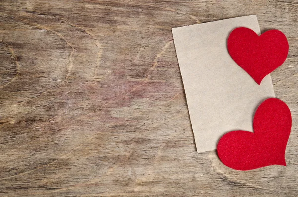 Two Red fabric hearts with sheet of paper lying on old wooden ba — Stock Photo, Image