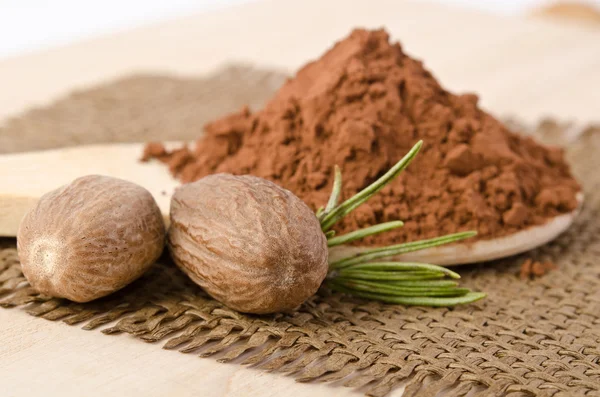 Nutmegs with a sprig of rosemary and cacao powder in the wooden — Stock Photo, Image