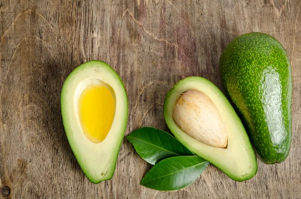 Aguacate fresco y aguacate como un tazón para el aceite en el backgro de madera — Foto de Stock