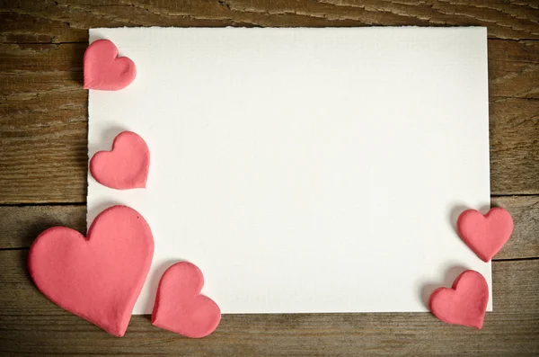 Carta bianca con piccoli cuori rosa sdraiati su uno sfondo di legno — Foto Stock