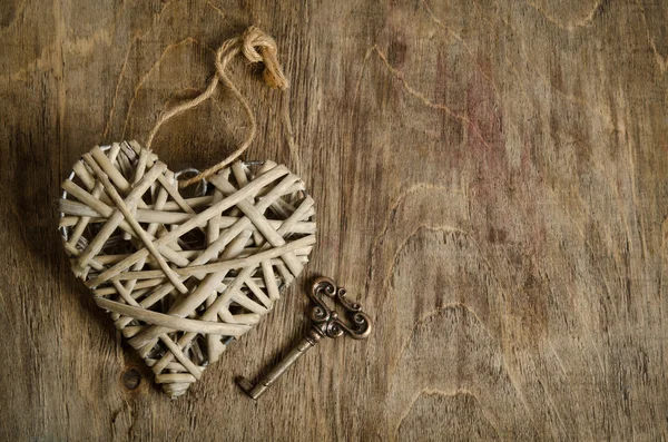 Corazón de mimbre hecho a mano con la llave acostada sobre una base de madera. arriba — Foto de Stock