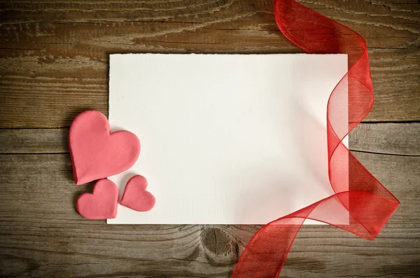 The piece of paper lying with hearts and ribbon on a wooden back — Stock Photo, Image