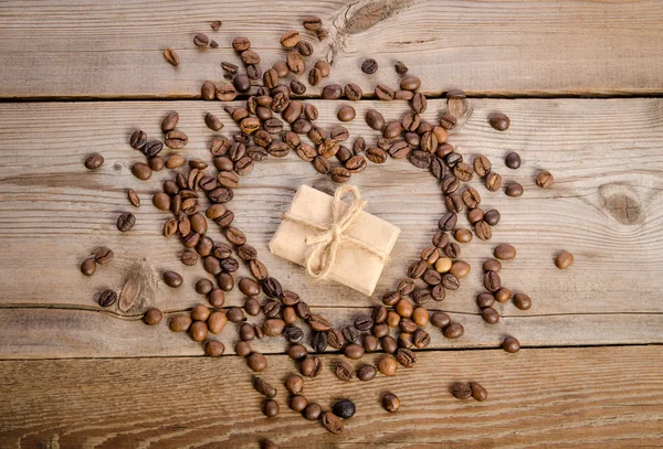 Frame- heart from coffee beans and small parcel inside it on  wo — Stock Photo, Image