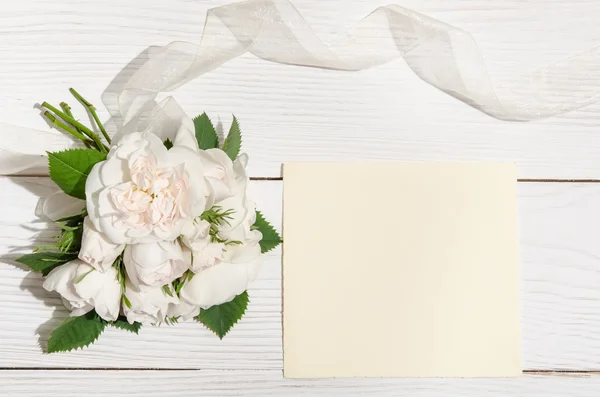 Білі троянди з порожньою карткою для тексту на білому столі. вид зверху — стокове фото