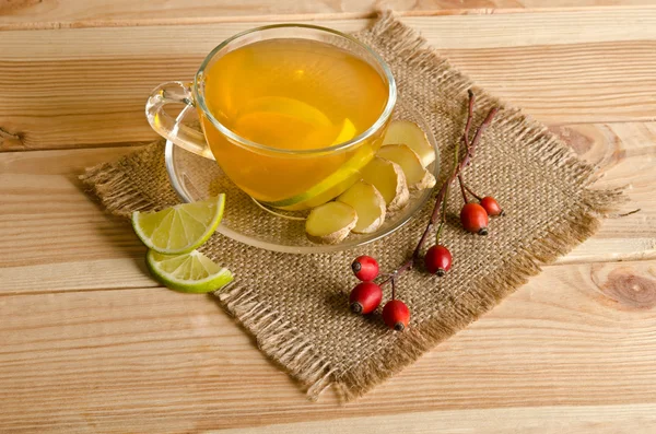 Чашка чая с ломтиками лимона и имбирем и ветками возле дикой розы — стоковое фото