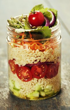 Bir kavanoz içinde salatalık, quinoa, domates, soğan, havuç ve naneli salata