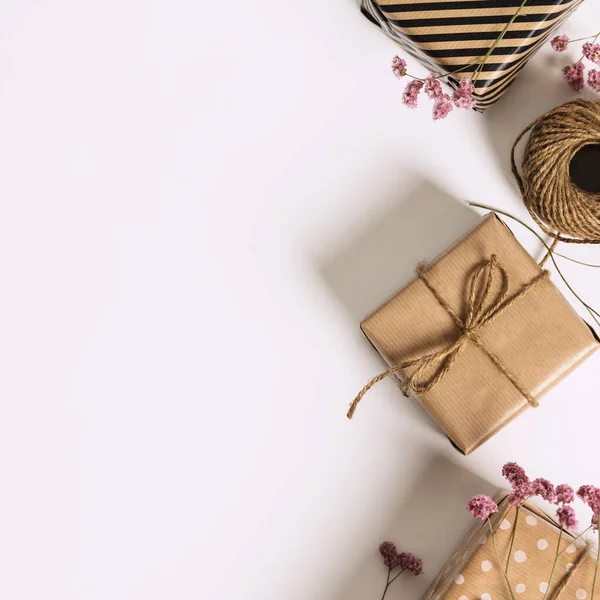 Gift box wrapped in kraft paper and pink flowers on white background. Flat lay styling. — Stock Photo, Image