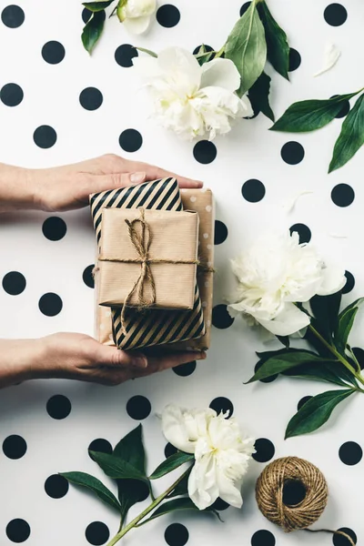Platt låg arrangemang honor händer håller presentförpackning bland presenter och blommor, ovanifrån — Stockfoto