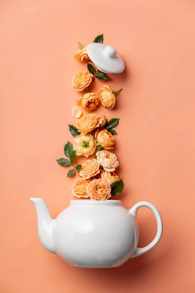 ピンクの背景にオレンジのバラと白いティーポットで作られた創造的なレイアウト — ストック写真