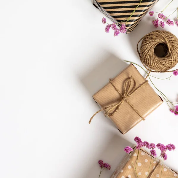 Gift box wrapped in kraft paper, notebook and pink flowers on white background. Flat lay styling. — Stock Photo, Image