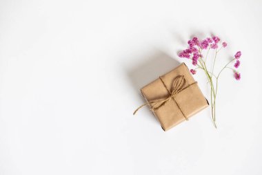 Kraft kağıdına sarılı bir hediye kutusu ve beyaz arka planda pembe çiçekler. Düz yatış stili.
