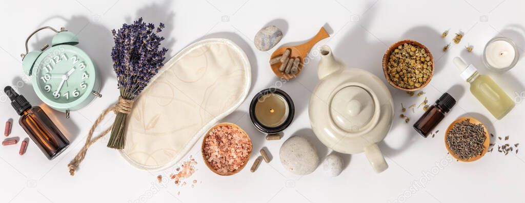 Herbal medicine for treat depression and insomnia concept. Alarm clock, medicine herbs, capsules, camomile tea and aromatherapy oil on white background, flat lay